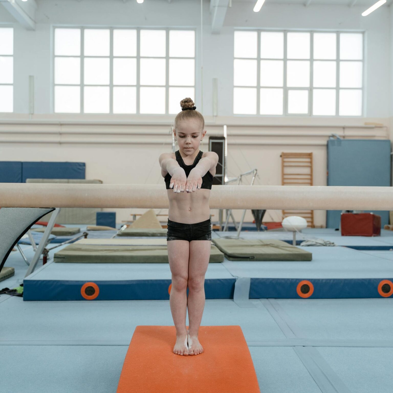 A young girl focuses while performing a balance beam routine in a gym. Gymnastics and training setting.