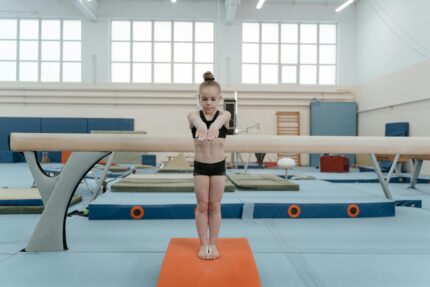 A young girl focuses while performing a balance beam routine in a gym. Gymnastics and training setting.