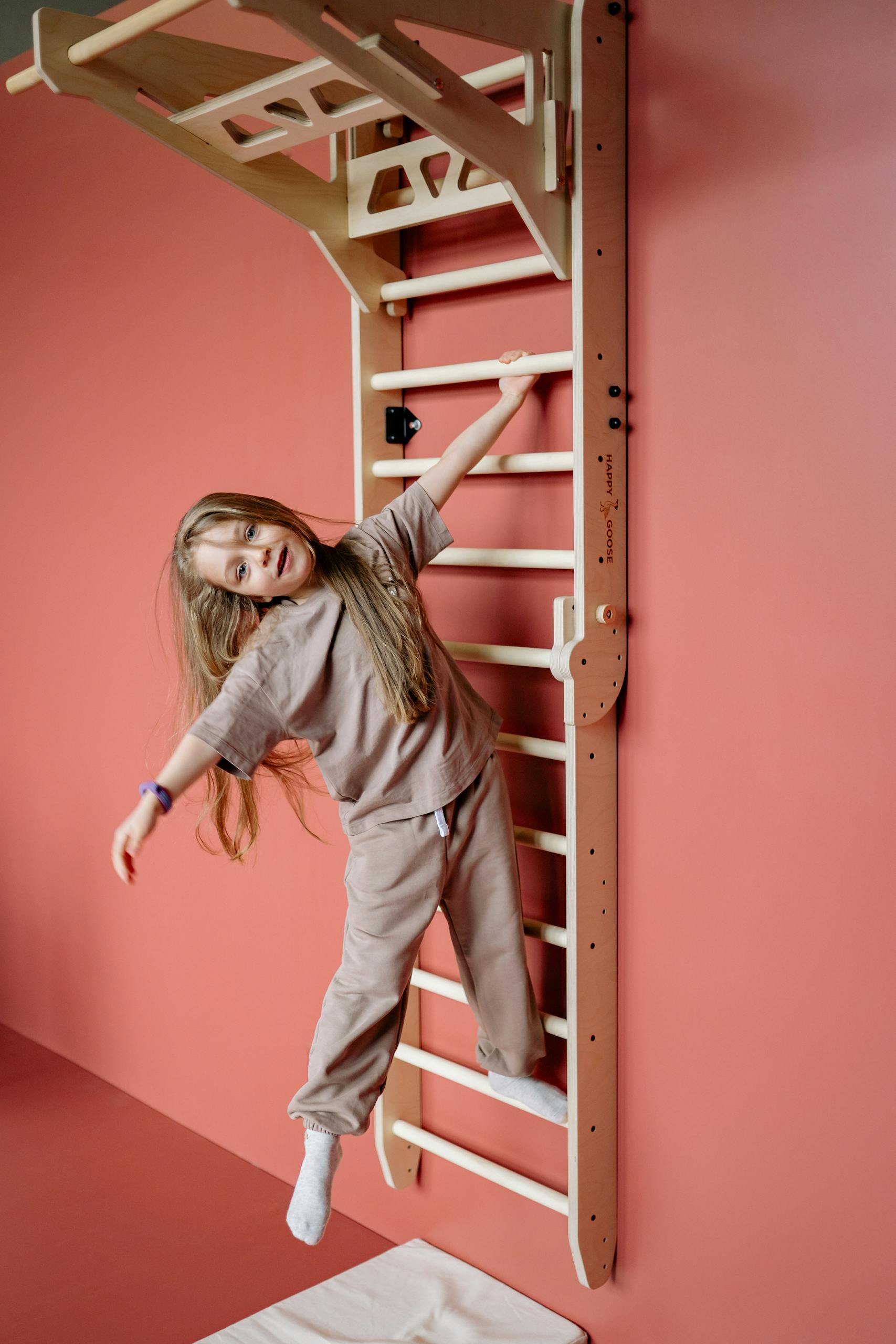 Cheerful young girl playing and climbing on a wooden gym ladder indoors.