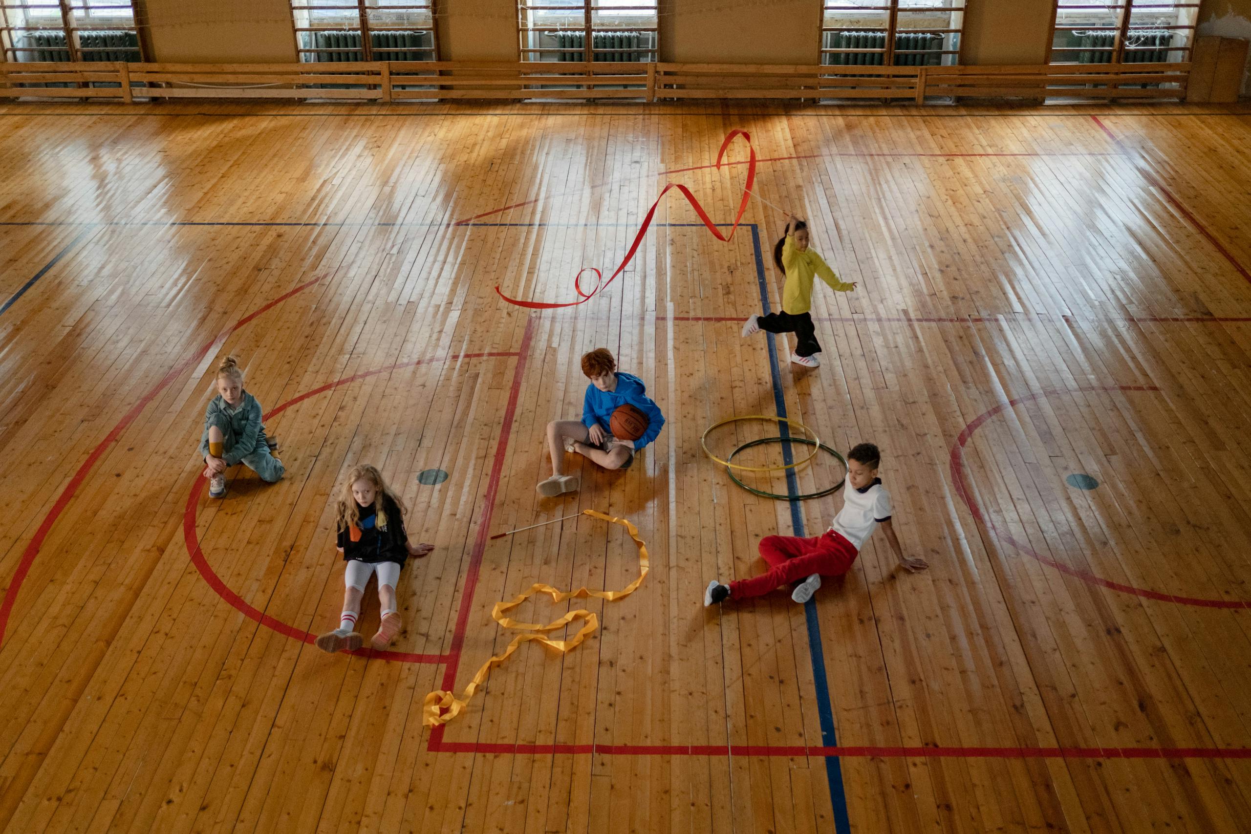 Children playing various games in an indoor gym with wooden floors, showcasing recreational fun.