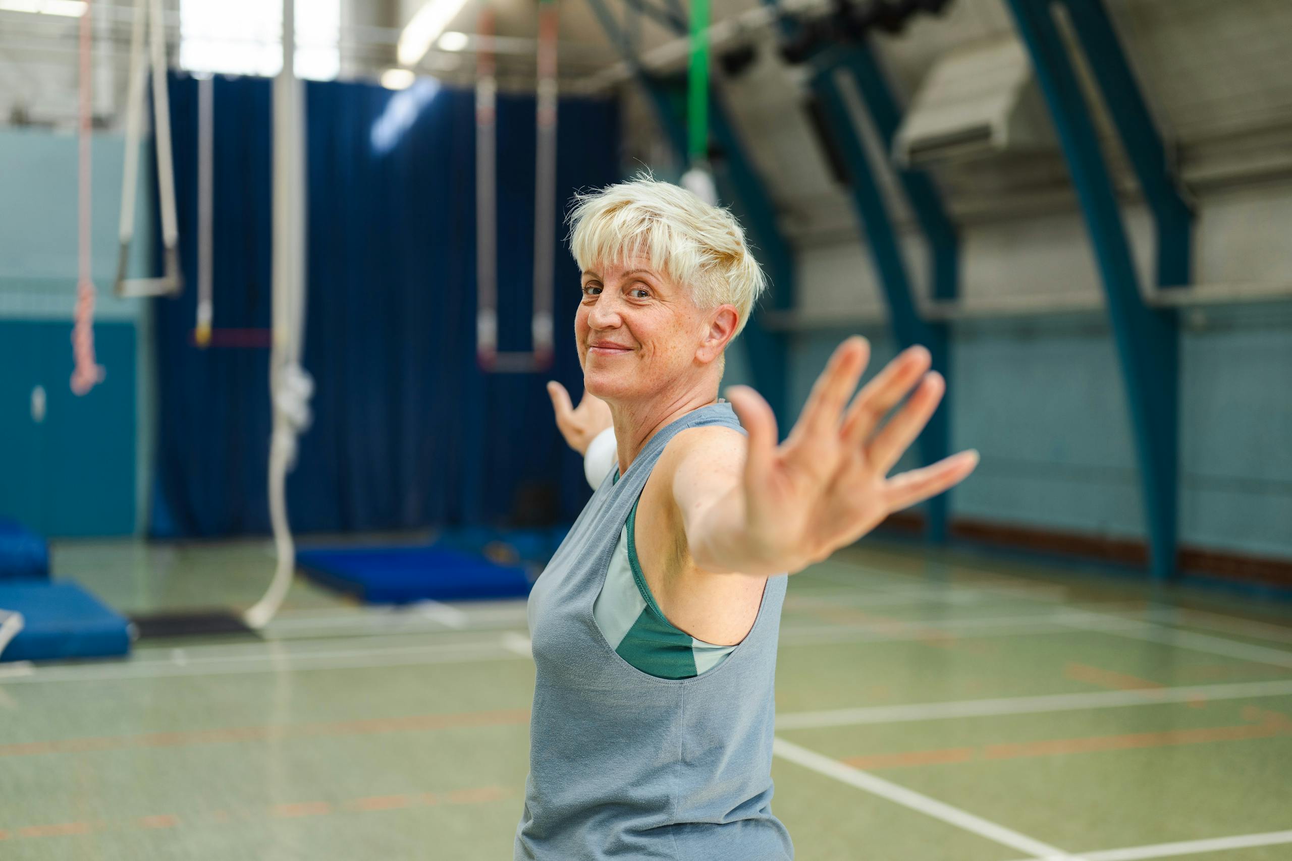 Senior woman with short blonde hair confidently stretching in a gymnasium setting, promoting active lifestyle.