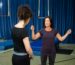 Two women engaged in a trapeze class inside a gym with mats and ropes.